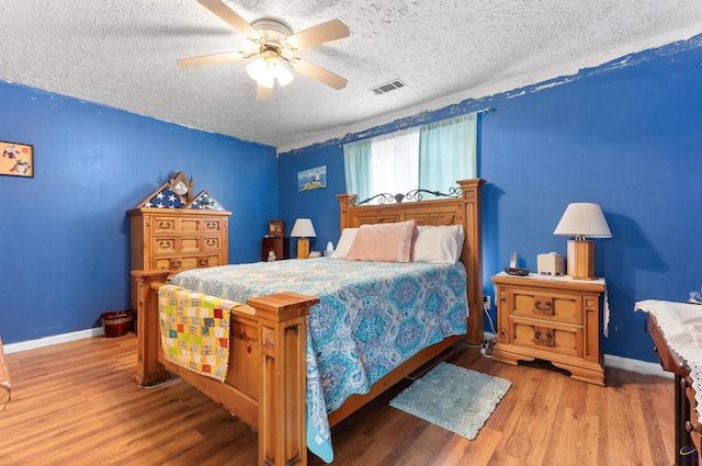 bedroom with visible vents, a textured ceiling, baseboards, and wood finished floors