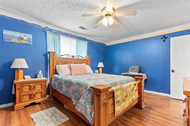 bedroom with visible vents, ceiling fan, a textured ceiling, wood finished floors, and baseboards