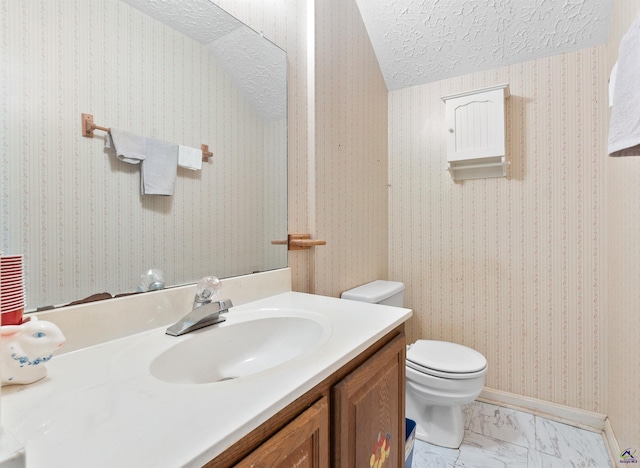 bathroom with a textured ceiling, toilet, vanity, marble finish floor, and wallpapered walls