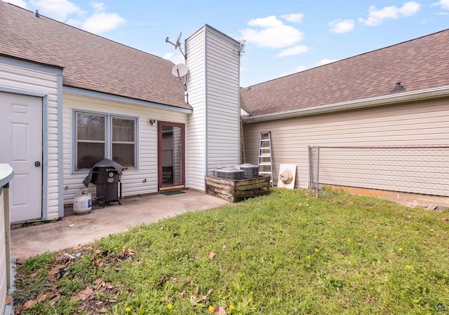 back of property with a shingled roof, a yard, a chimney, and a patio