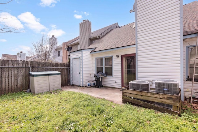 back of property with a yard, a chimney, central air condition unit, a shingled roof, and a fenced backyard