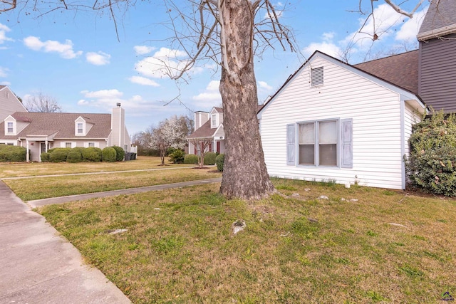 view of side of property with a shingled roof and a lawn