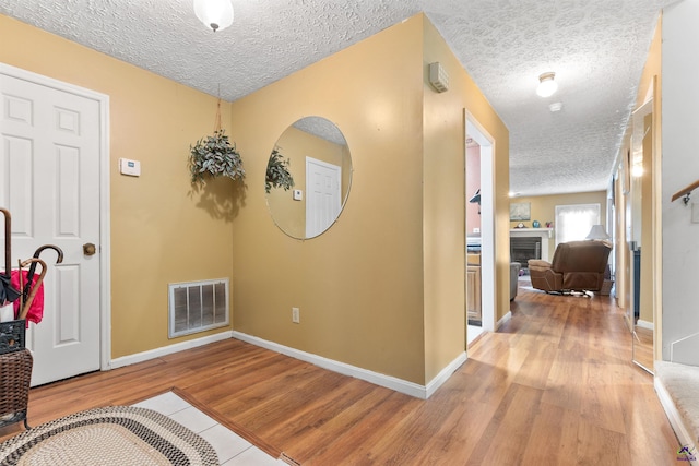 corridor with light wood-type flooring, baseboards, visible vents, and a textured ceiling