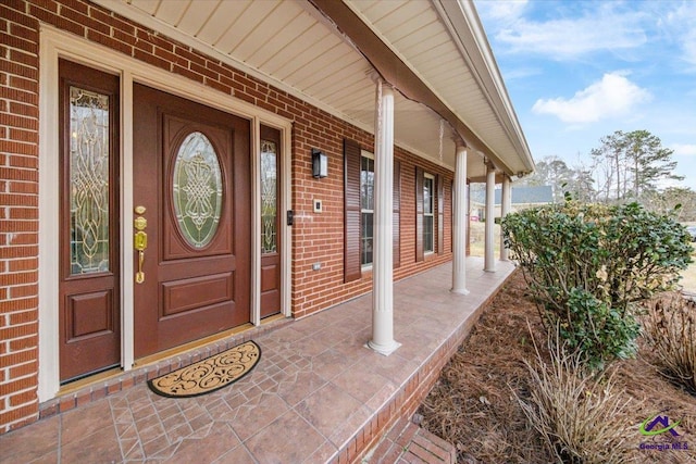 doorway to property with covered porch and brick siding