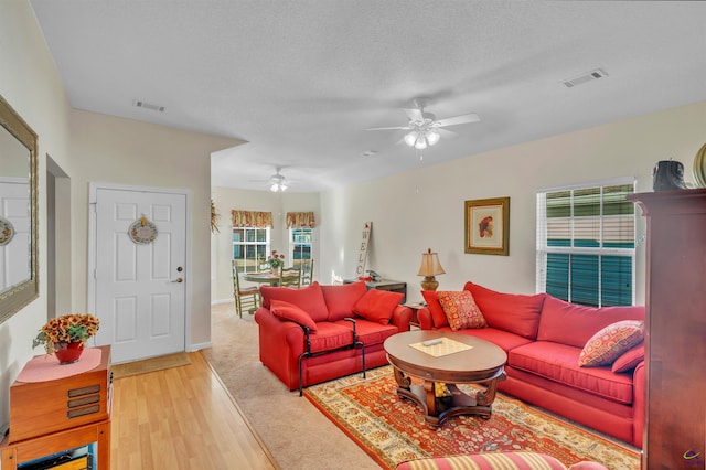 living area with light wood finished floors, a ceiling fan, visible vents, and a textured ceiling