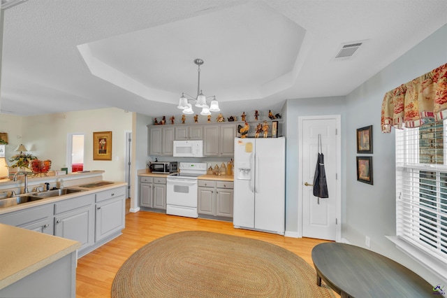 kitchen featuring light wood-style flooring, white appliances, a sink, visible vents, and a tray ceiling