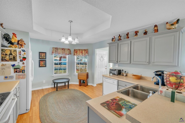 kitchen featuring white appliances, a sink, light countertops, light wood finished floors, and a raised ceiling