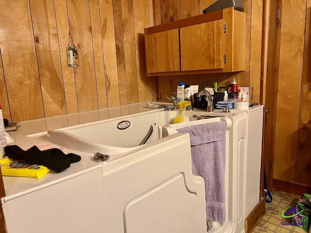 clothes washing area featuring cabinet space, wooden walls, and light floors