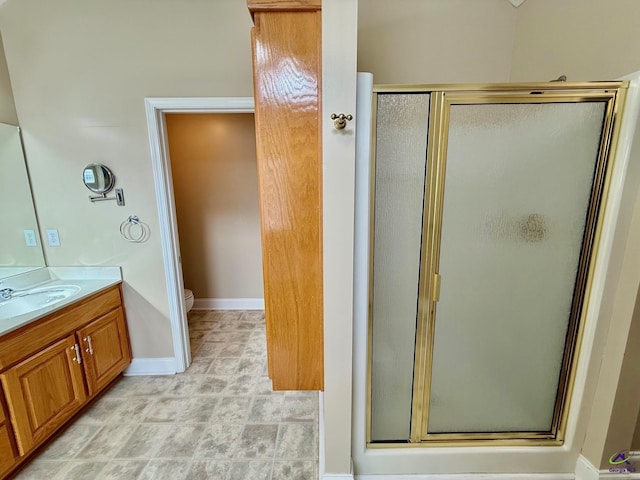 bathroom featuring toilet, a stall shower, vanity, and baseboards