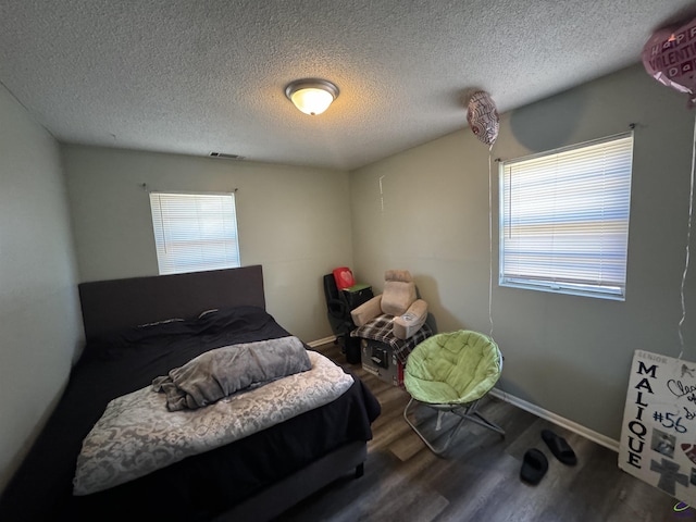 bedroom featuring baseboards, a textured ceiling, visible vents, and wood finished floors