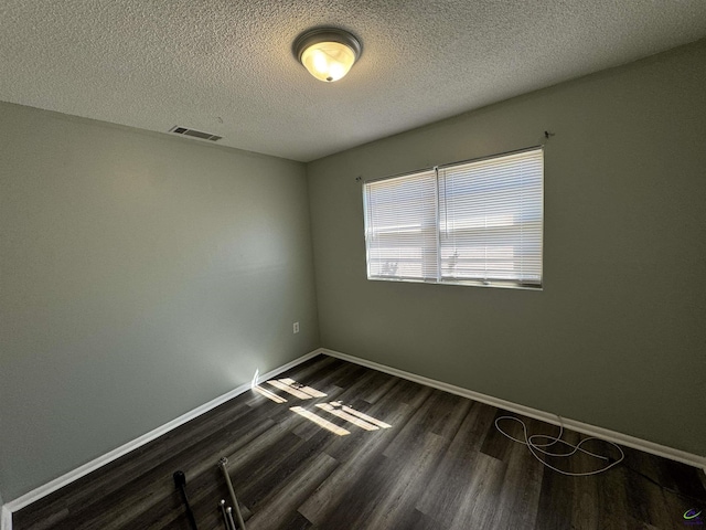 spare room featuring dark wood-style flooring, visible vents, a textured ceiling, and baseboards