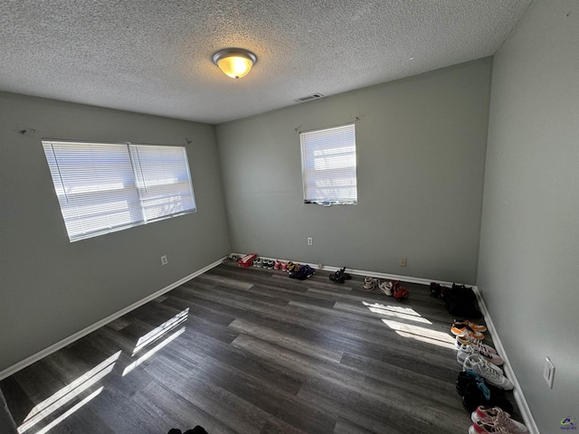 unfurnished room with baseboards, a textured ceiling, visible vents, and wood finished floors