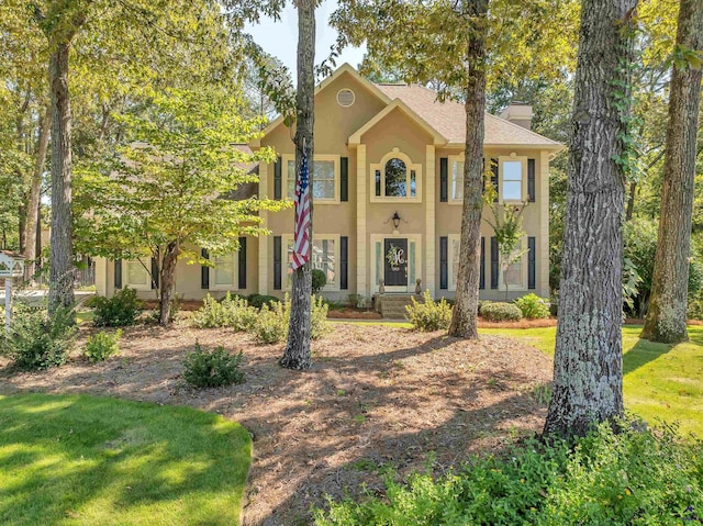 colonial-style house with a chimney, a front lawn, and stucco siding