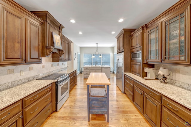 kitchen with decorative backsplash, light wood-style flooring, glass insert cabinets, appliances with stainless steel finishes, and pendant lighting