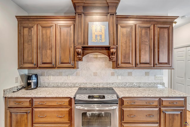 kitchen with light stone countertops, stainless steel range with electric stovetop, tasteful backsplash, and brown cabinetry