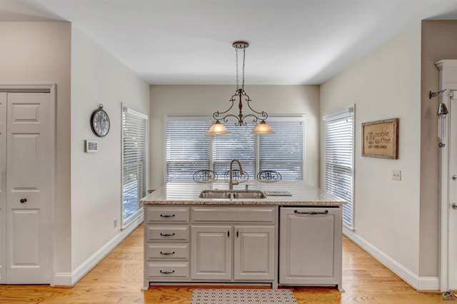 kitchen with paneled dishwasher, decorative light fixtures, a sink, and light wood finished floors