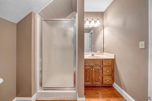 bathroom featuring a stall shower, a textured ceiling, vanity, wood finished floors, and baseboards