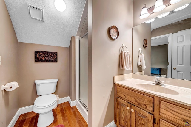 bathroom featuring a textured ceiling, toilet, wood finished floors, baseboards, and a stall shower