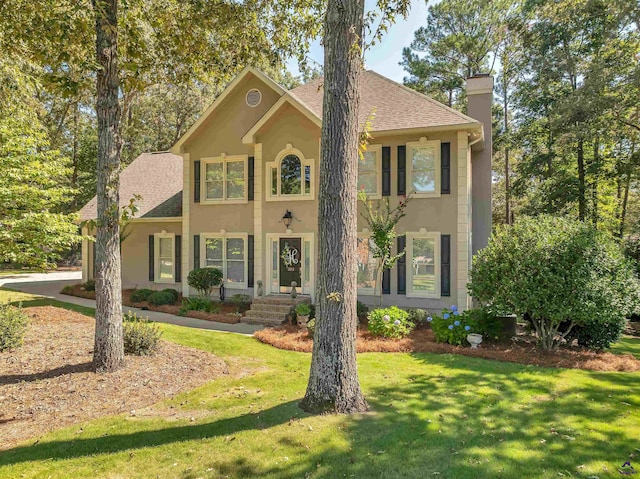 colonial house with a front lawn, a chimney, a shingled roof, and stucco siding