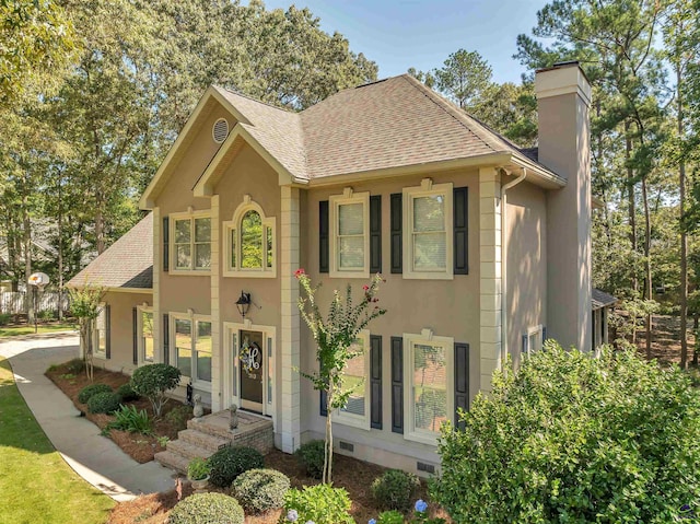 colonial house with crawl space, roof with shingles, a chimney, and stucco siding