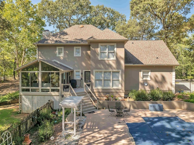 rear view of house with roof with shingles, a chimney, stucco siding, a sunroom, and a patio area