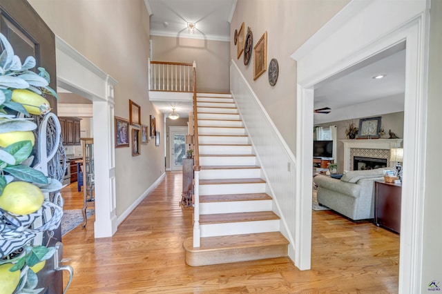 stairs with baseboards, a tiled fireplace, a towering ceiling, ornamental molding, and wood finished floors