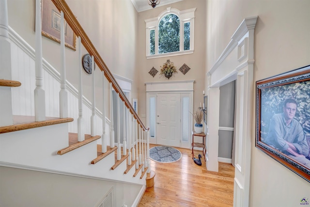 foyer featuring a high ceiling, ornamental molding, wood finished floors, baseboards, and stairs