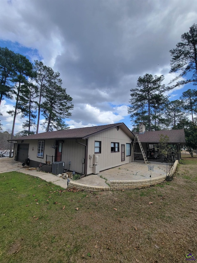 back of house with central AC unit, a lawn, a chimney, an attached garage, and a patio area