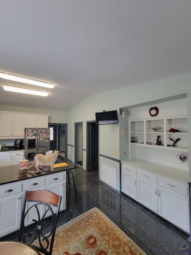 kitchen featuring a textured ceiling, granite finish floor, white cabinets, and stainless steel fridge with ice dispenser
