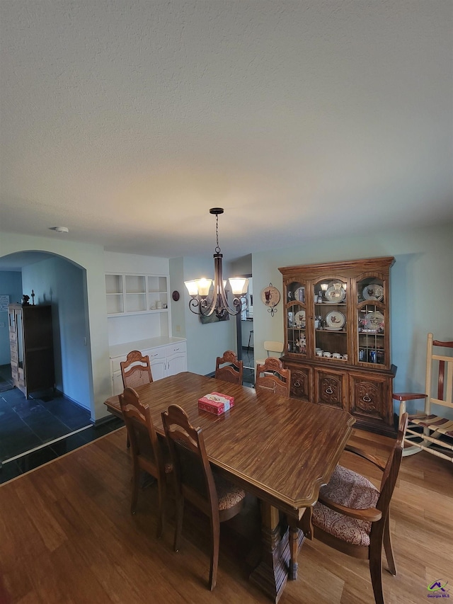 dining space with a chandelier, arched walkways, a textured ceiling, and wood finished floors