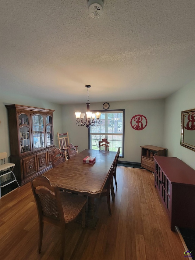 dining space with an inviting chandelier, a textured ceiling, and wood finished floors