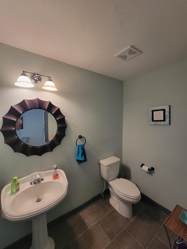 half bathroom with baseboards, visible vents, toilet, a textured ceiling, and a sink