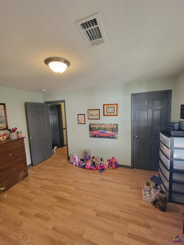 rec room featuring light wood-style floors, visible vents, and a textured ceiling