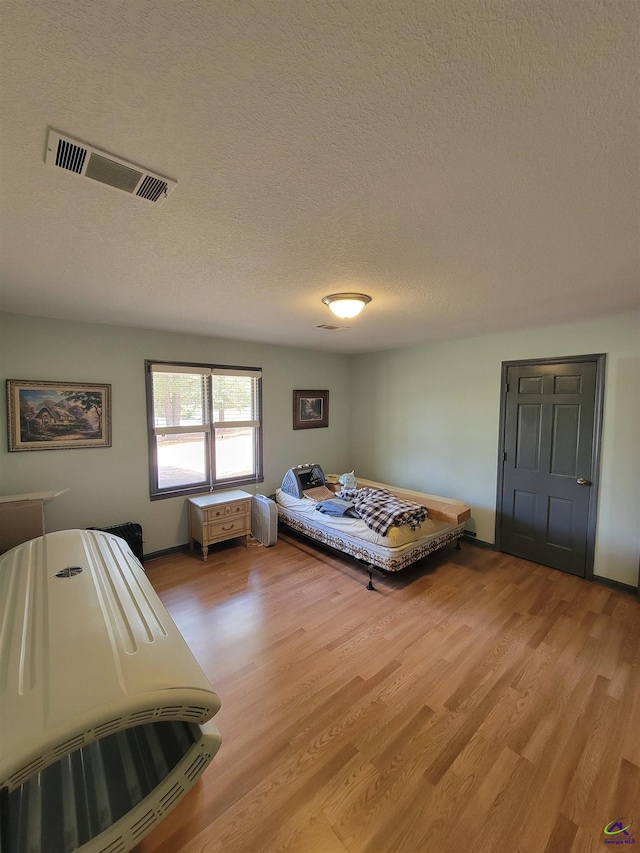 bedroom with light wood-style floors, visible vents, and a textured ceiling
