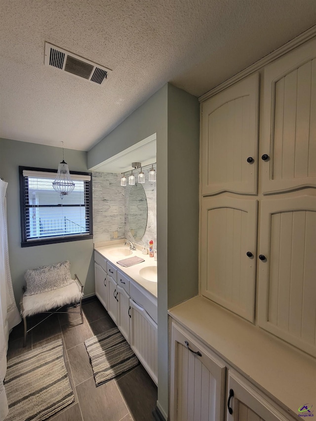 bathroom with double vanity, a sink, visible vents, and a textured ceiling