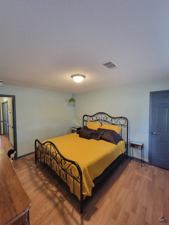 bedroom featuring baseboards, a textured ceiling, visible vents, and wood finished floors