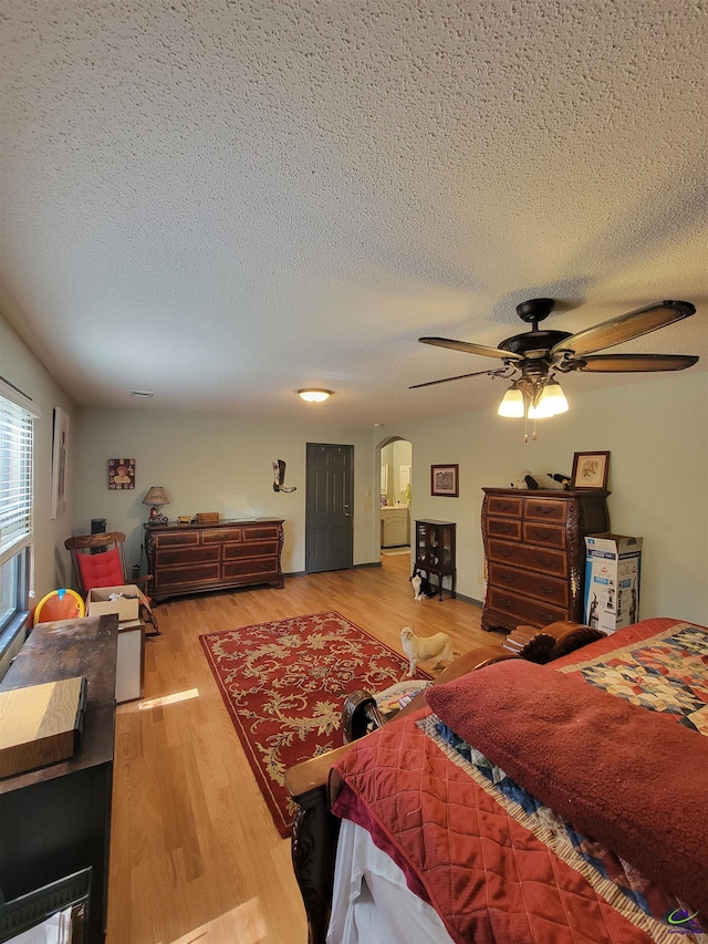 bedroom with ceiling fan, a textured ceiling, arched walkways, and wood finished floors