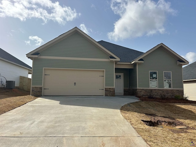 craftsman house with an attached garage, cooling unit, a shingled roof, stone siding, and concrete driveway