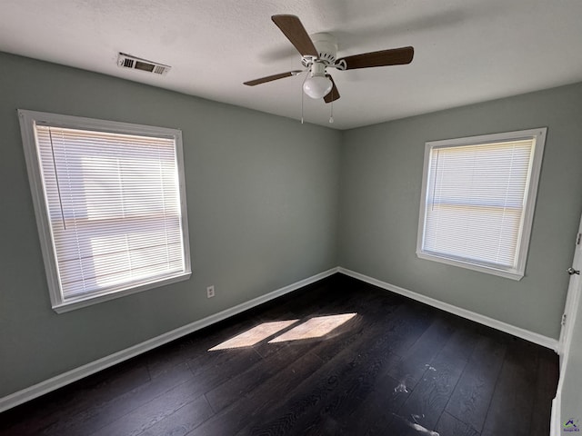 unfurnished room featuring dark wood-style floors, a ceiling fan, visible vents, and baseboards