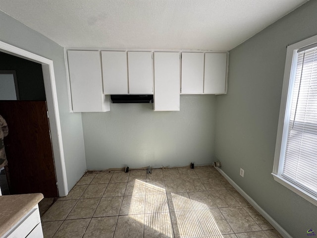 kitchen featuring baseboards, under cabinet range hood, light tile patterned flooring, and white cabinets