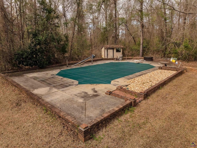 view of pool featuring a storage shed, a patio, a covered pool, an outbuilding, and a diving board