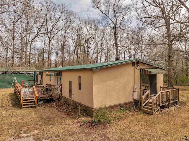 view of home's exterior with crawl space, metal roof, a deck, and stucco siding