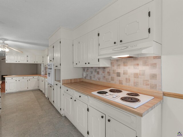 kitchen featuring white appliances, under cabinet range hood, white cabinetry, and backsplash