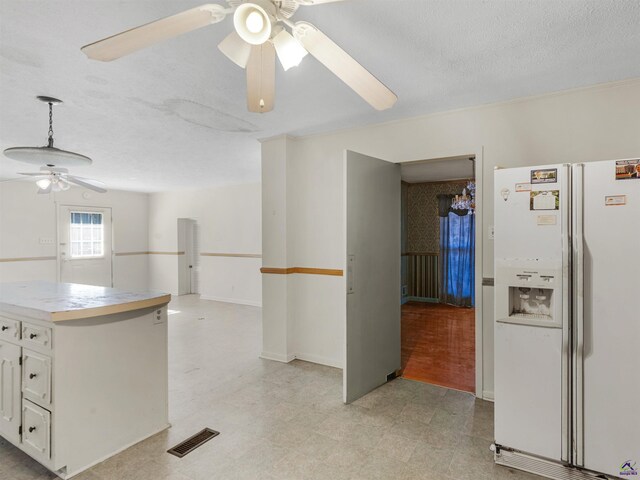 kitchen with white refrigerator with ice dispenser, light countertops, visible vents, white cabinetry, and a textured ceiling