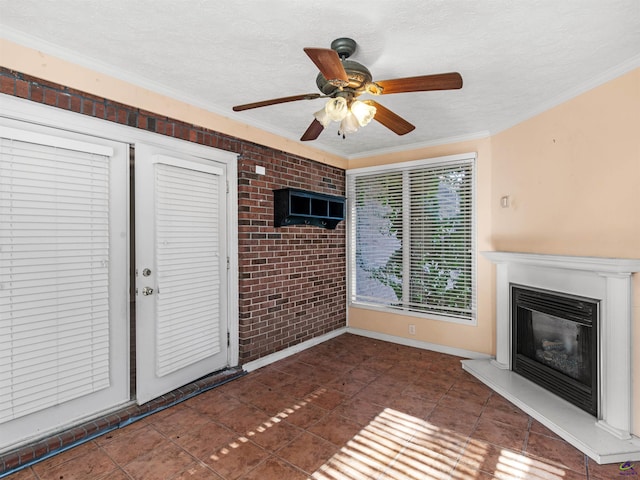 unfurnished living room featuring a textured ceiling, ceiling fan, brick wall, ornamental molding, and a glass covered fireplace