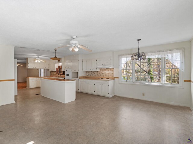 kitchen featuring under cabinet range hood, white cabinets, white oven, a center island, and stovetop