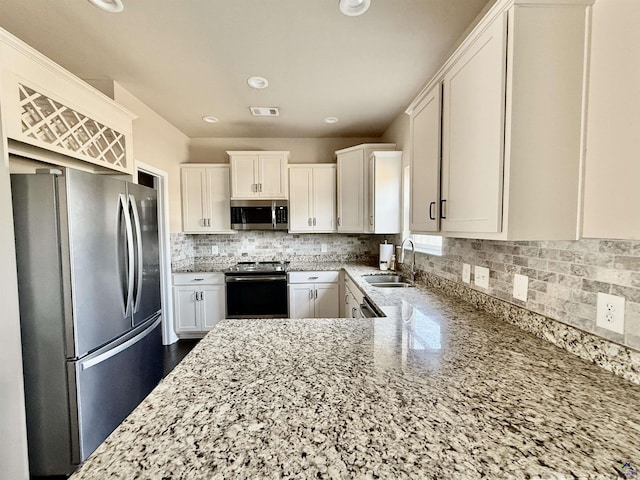 kitchen featuring light stone counters, stainless steel appliances, tasteful backsplash, visible vents, and a sink