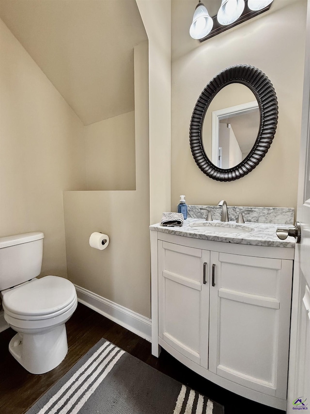 bathroom with toilet, wood finished floors, vanity, baseboards, and vaulted ceiling