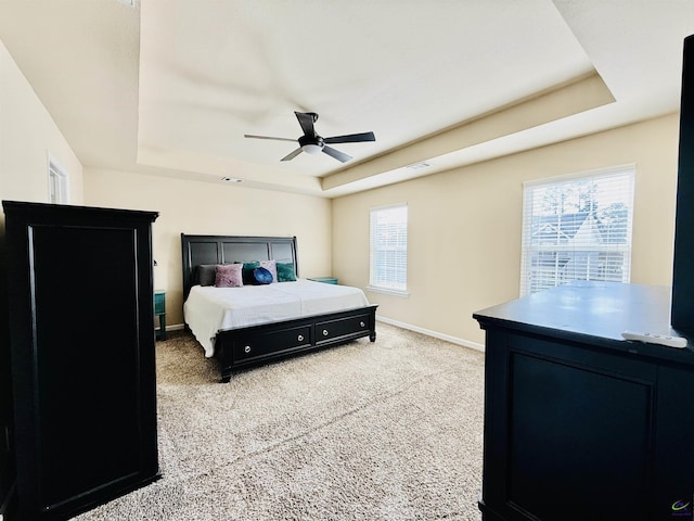 bedroom with a ceiling fan, a raised ceiling, light colored carpet, and baseboards