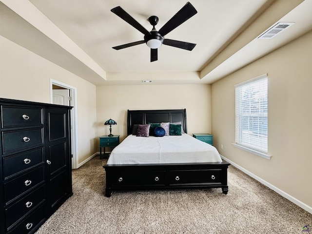 bedroom with light carpet, a tray ceiling, visible vents, and baseboards